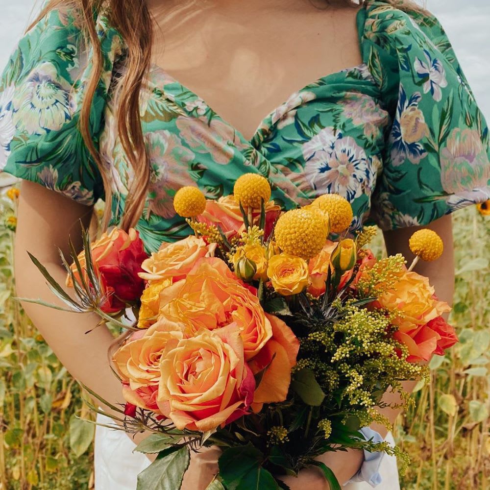 woman n floral puff sleeve top holding orange flowers