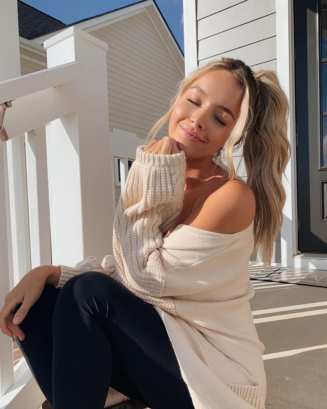 woman in off the shoulder sweater with a ponytail smiling in the sun outside