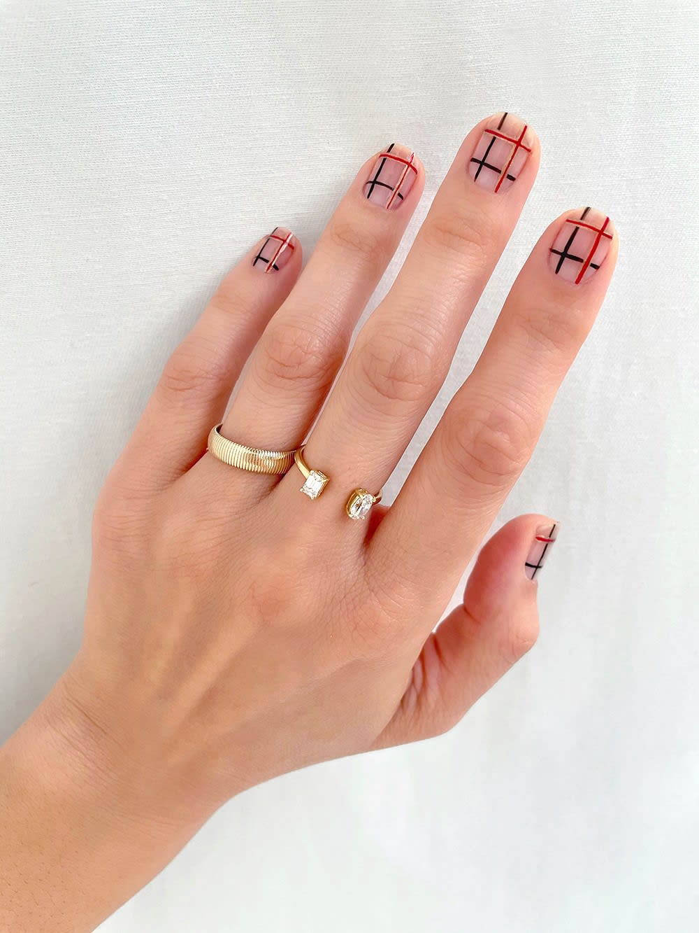 red, black, and gold plaid nails for holiday on a hand wearing gold rings