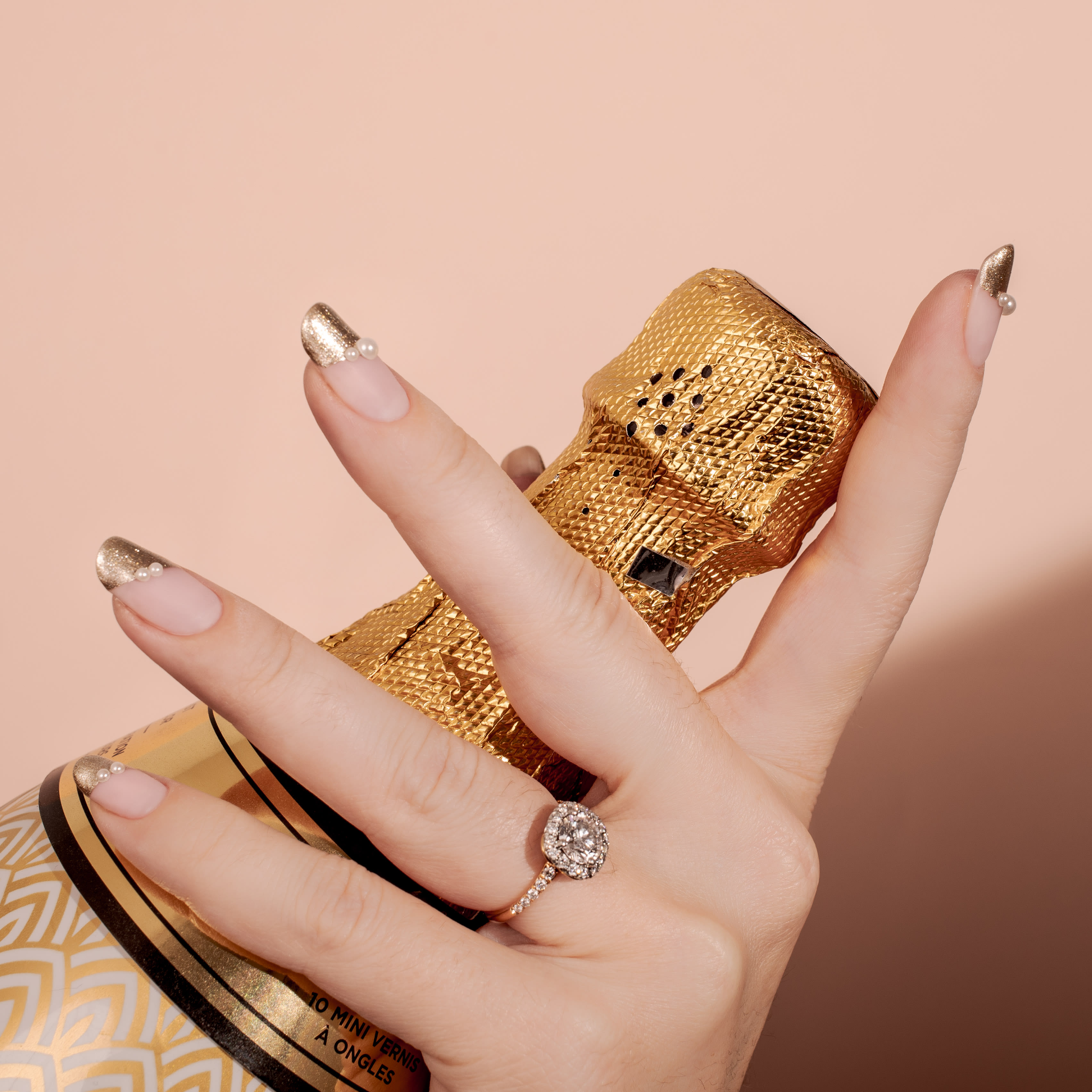 a hand holding a champagne botttle with gold tip wedding nails with pearl detail