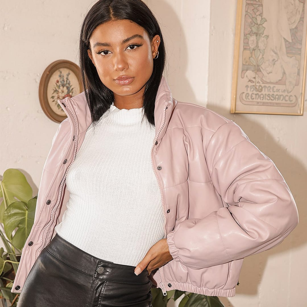 a woman wearing a white tee and black leather pants with a mauve pink cropped puffer jacket in vegan leather with her hand on her hip