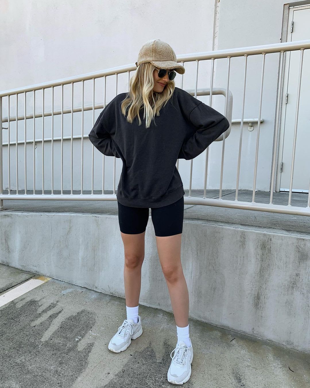 a blonde woman wearing a sherpa baseball cap and a sweatshirt and bike shorts with sneakers for fitness