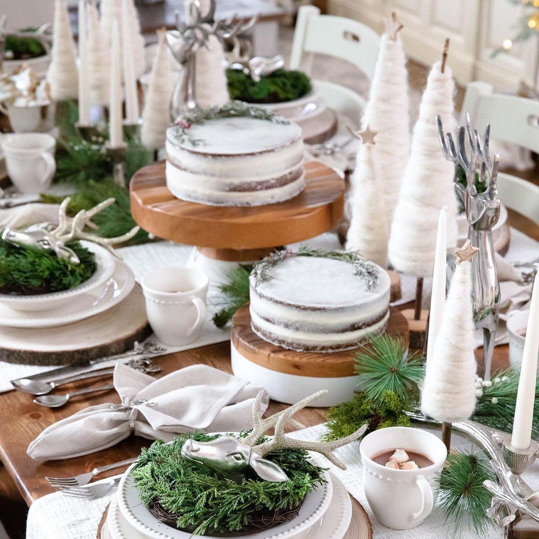 white and evergreen christmas tablescape with silver reindeer decorations and naked cakes and white trees