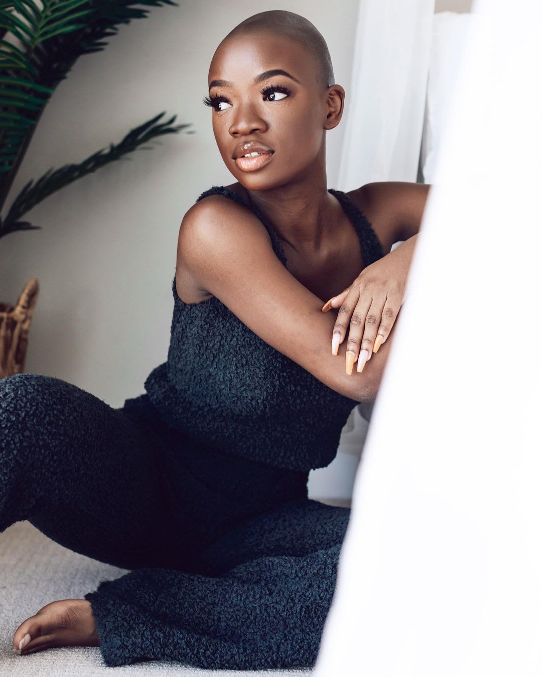 a woman in a black fuzzy loungewear set sitting on the floor looking outward