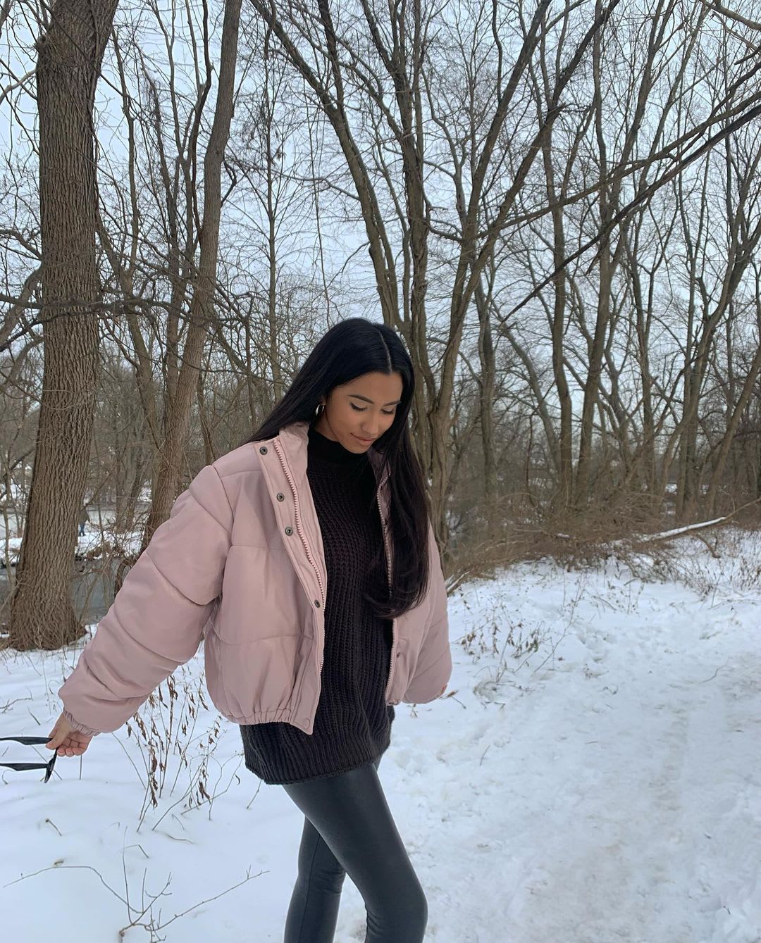 a woman walking in the snow as outdoor winter activity, wearing a mauve puffer jacket and black outfit