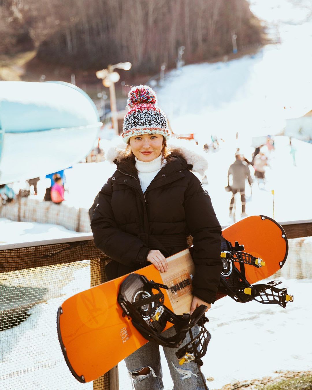 a woman wearing a black parka and knit beanie holding a snowboard for outdoor winter activity