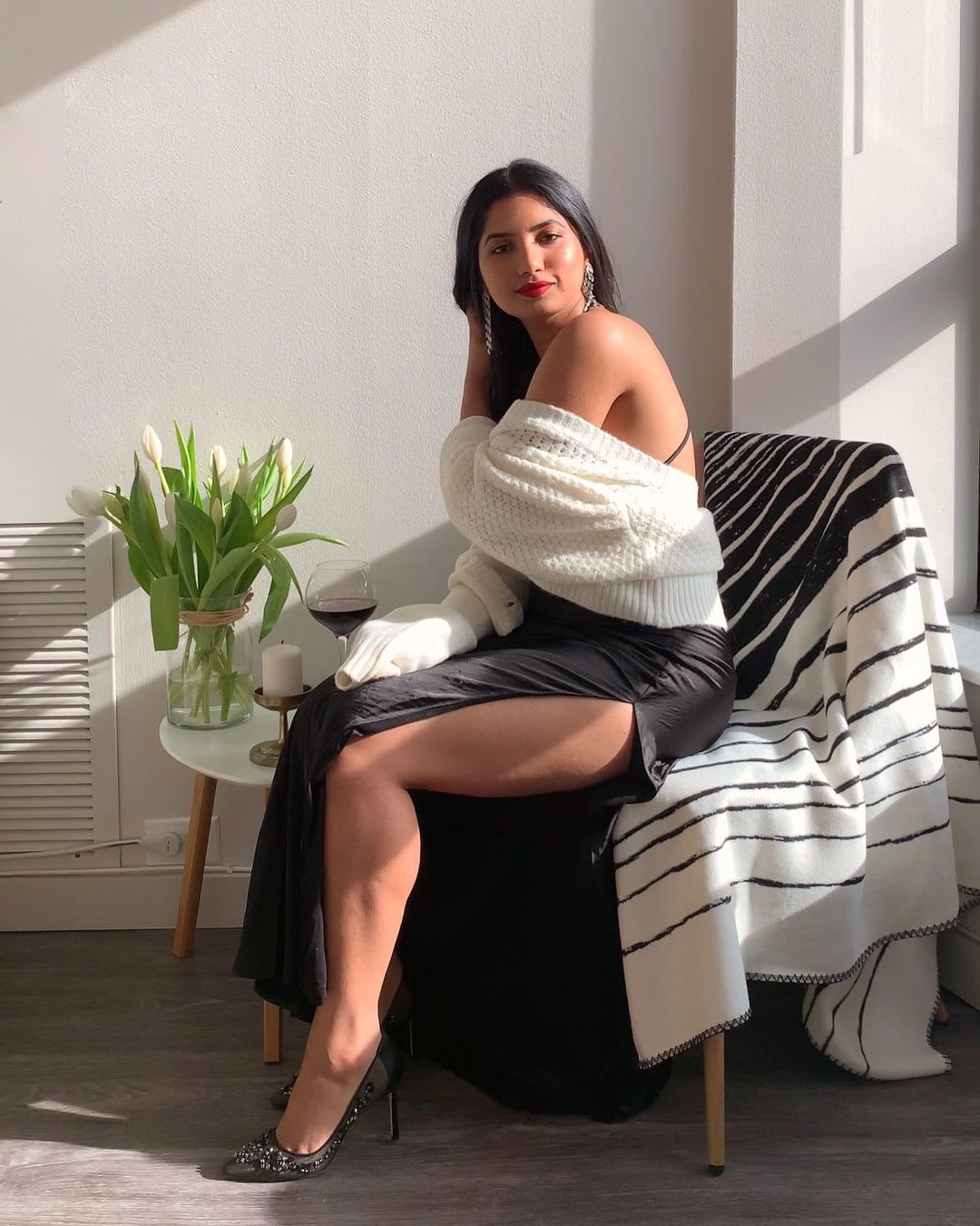 a woman sitting wearing a maxi dress with a cardigan and wine glass sitting by a window
