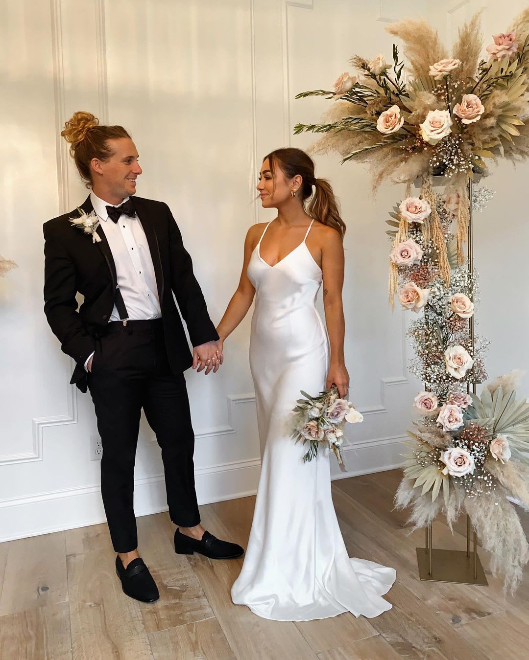 a bride and groom in wedding attire near a flower arch