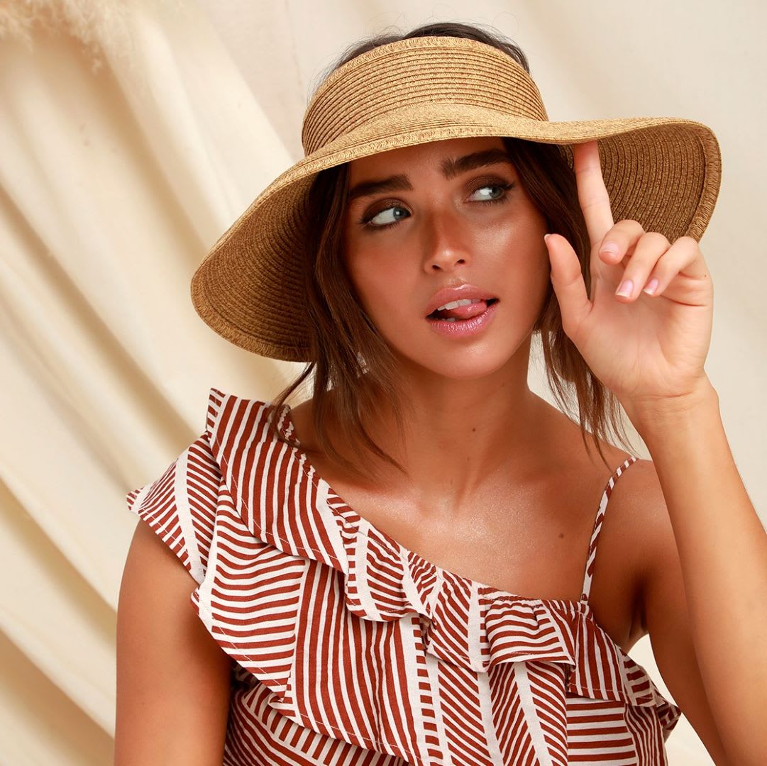 a woman wearing a straw visor and a one shoulder ruffle stripe jumpsuit