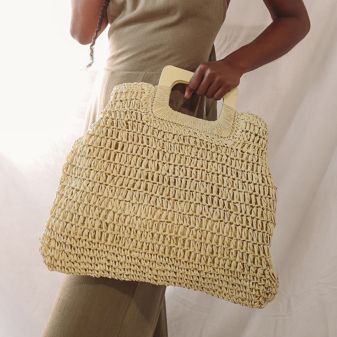 a woman in a green dress holding a beige woven oversized tote bag