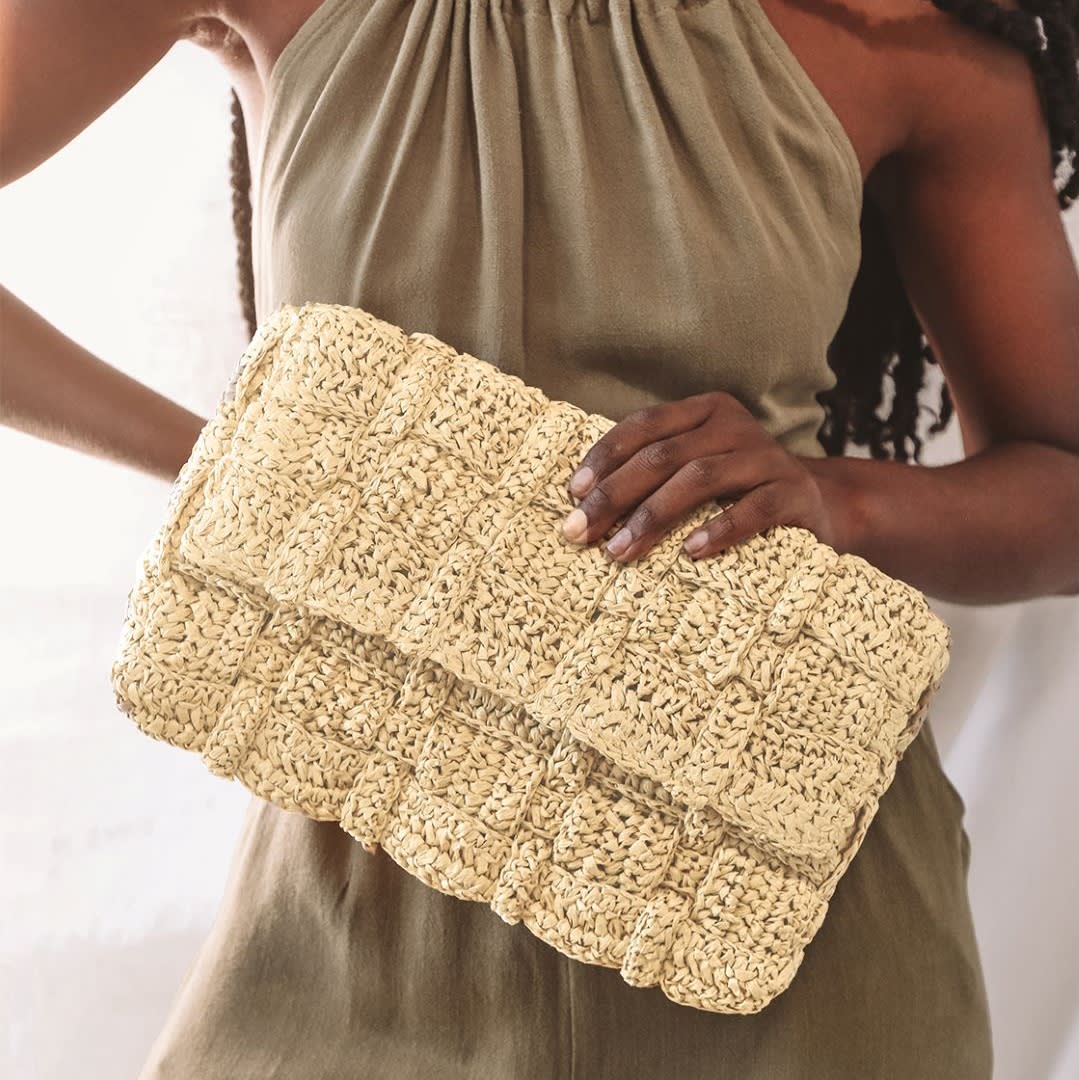 a woman holding a beige oversized straw clutch bag