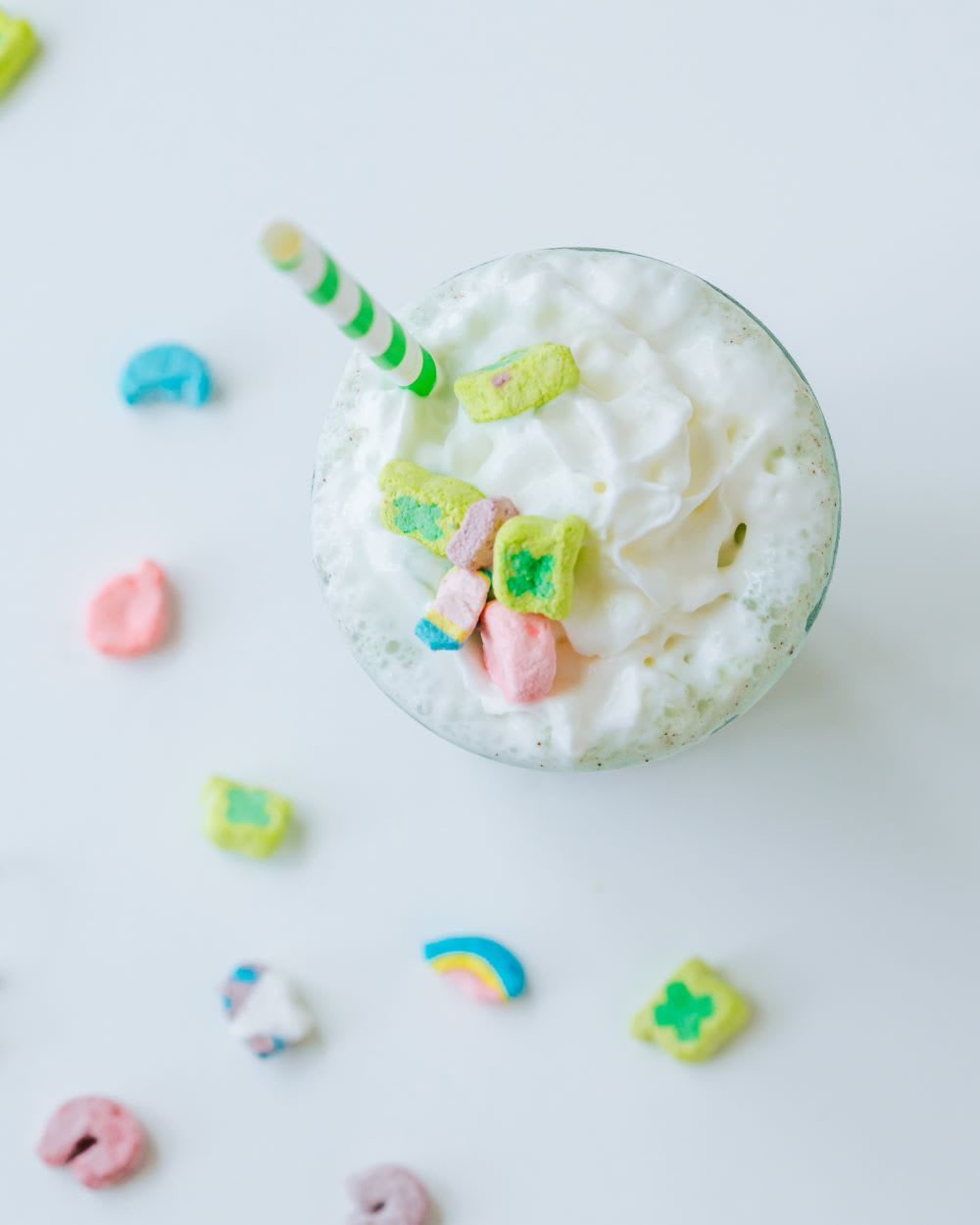 overhead view of boozy milkshake with lucky charms and green and white striped straw