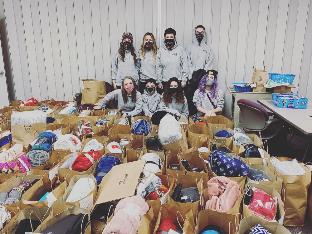 project 48 team posing with boxes of new clothing and toiletries donations