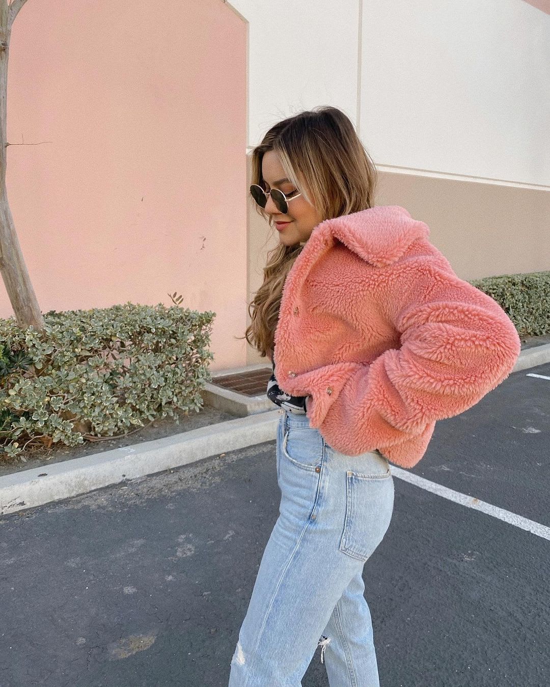 a woman in a fuzzy pink jacket and high wiasted jeans walking though a parking lot as an example of changing daily habits