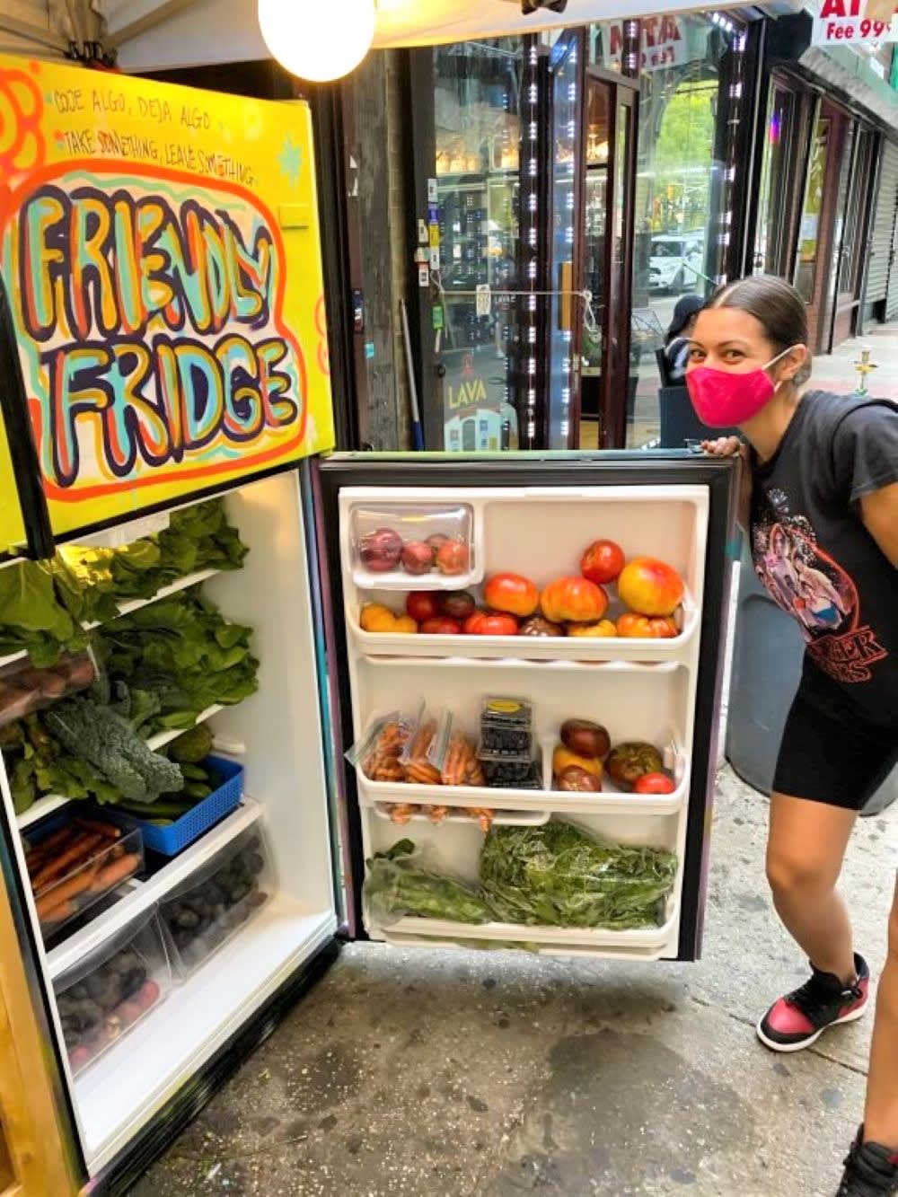 a woman poses wih an open community fridge full of food