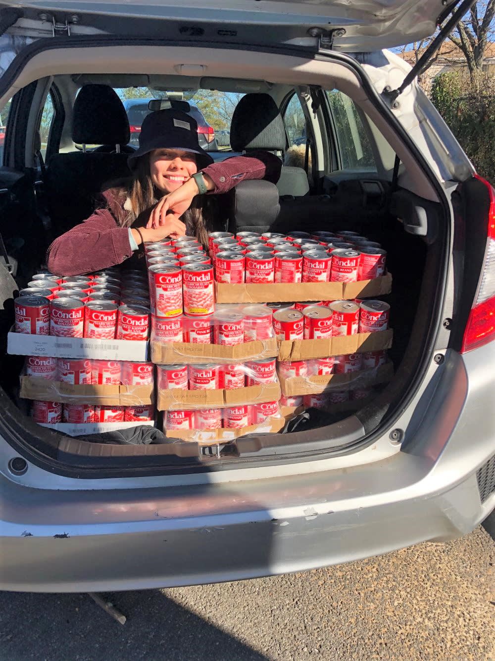 a woman posing with mutual aid supplies for community fridge in the back of a van