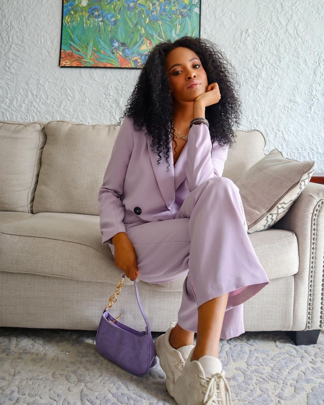 a woman in a lilac pant suit sitting on a couch with her head in her hand and legs crossed