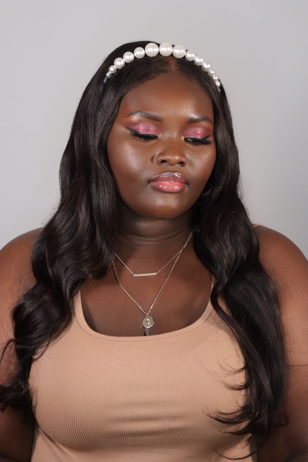 a woman wearing a pearl beaded headband and layered gold necklace with spring makeup with soft pink gloss and layered pink eyeshadow