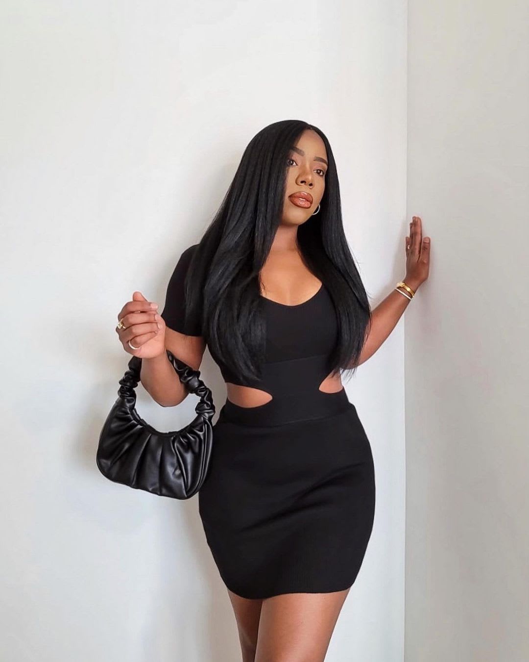 a woman wearing a black side-cutout dress and holding a ruched black bag