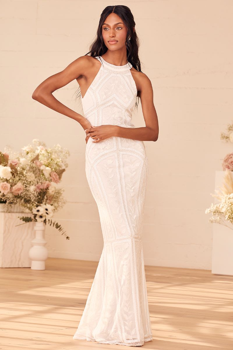 a model wearing a white beaded sequin halter maxi dress with one hand on her hip and other across her waist