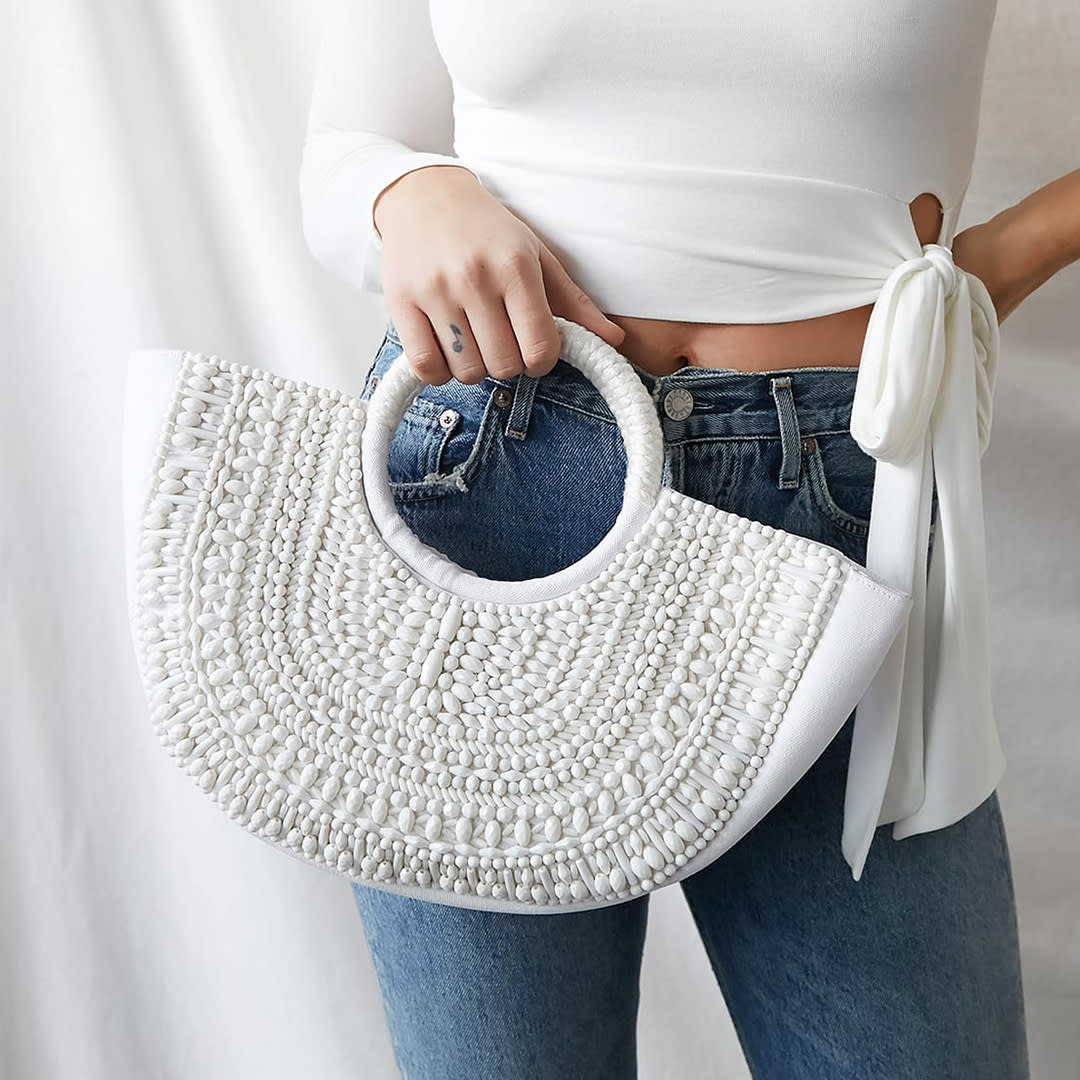 a hand holding a white beaded tote