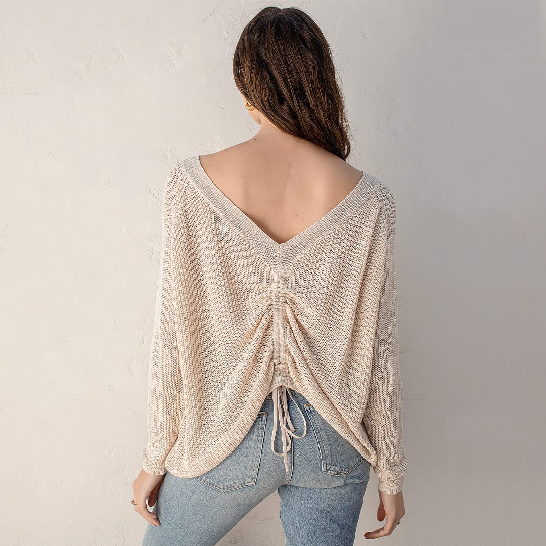 a back view of a woman wearing a beige reversible sweater top with ruching down the center