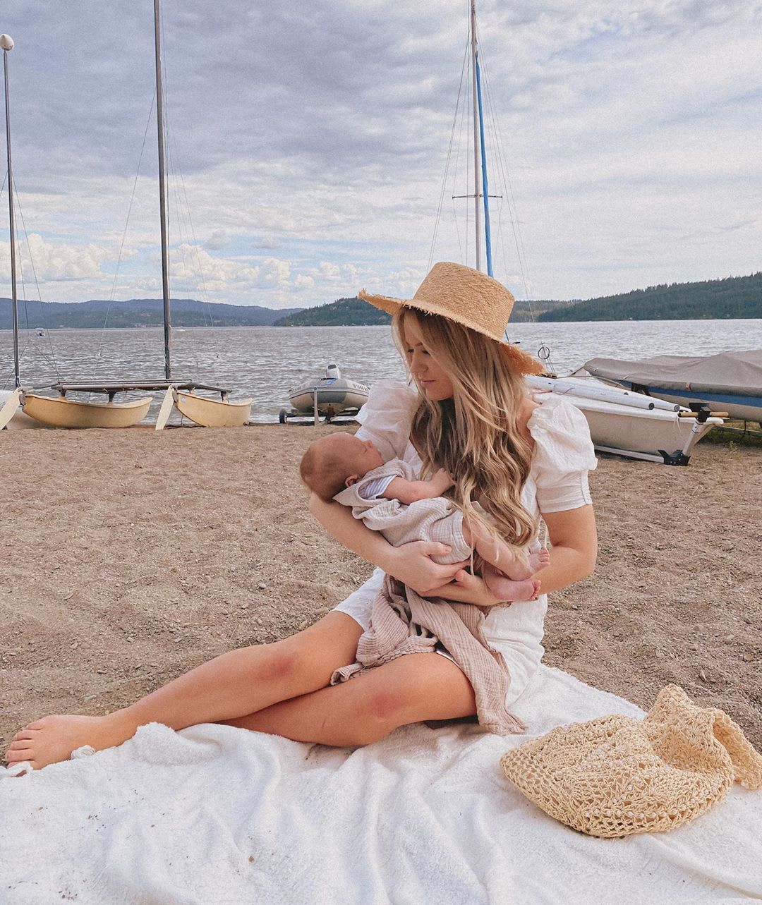 a woman sitting on the beach in front of boats parenting a baby