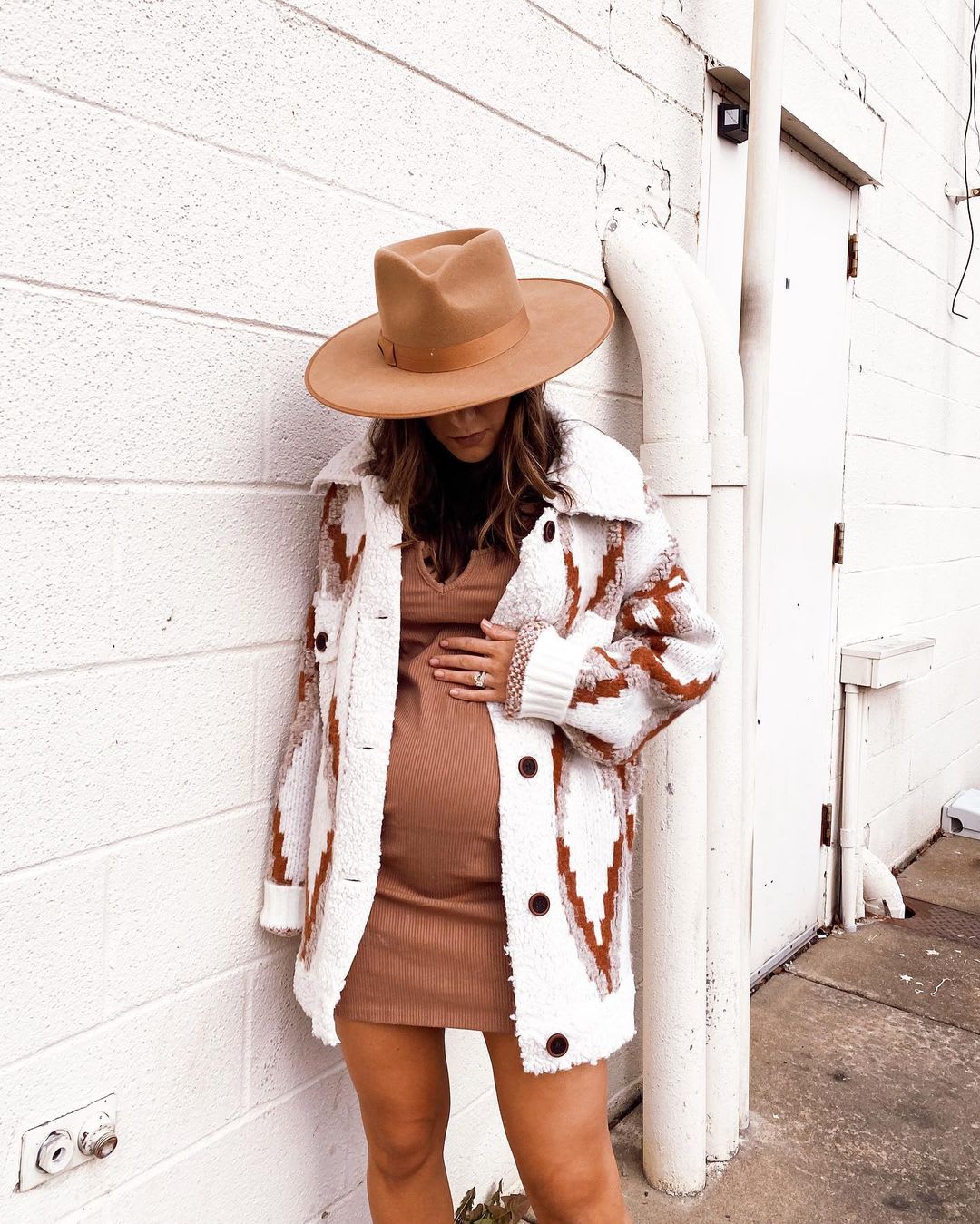 a pregnant woman in a bump-friendly knit dress with a cardigan sweater and wide brim hat considering parenting advice