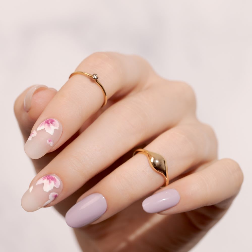 a hand bent to show off mismatched solid lavender and negative space flower nails in white and pink