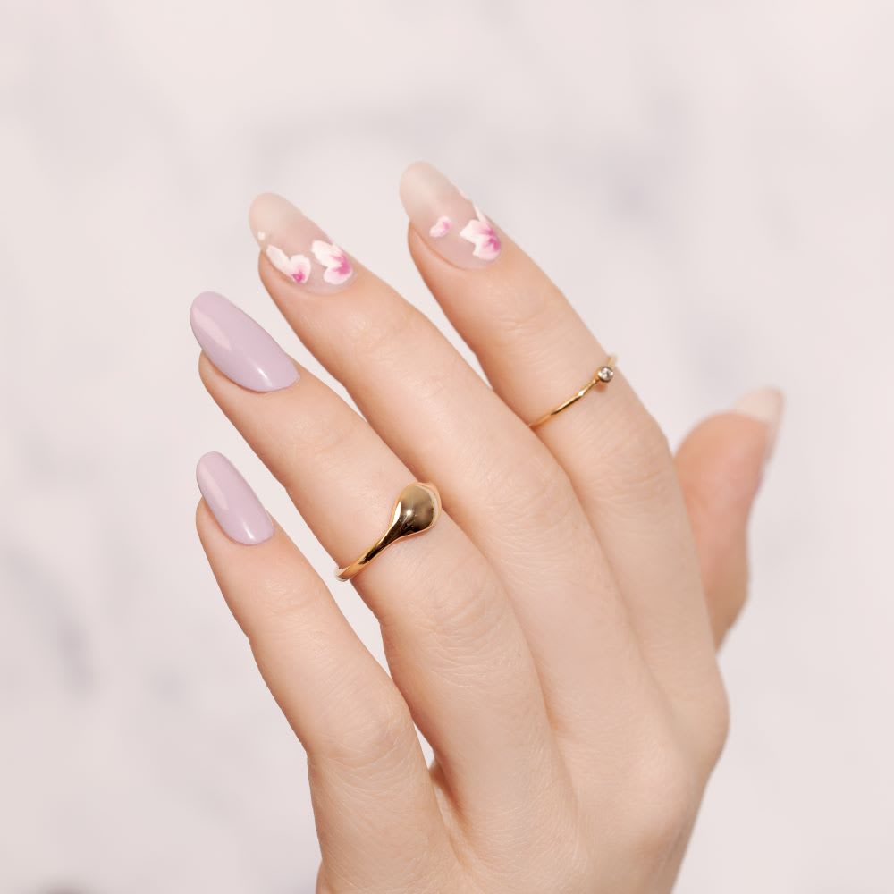 a hand wearing gold rings from lulus with mismatched solid and flower nails in lavender and white