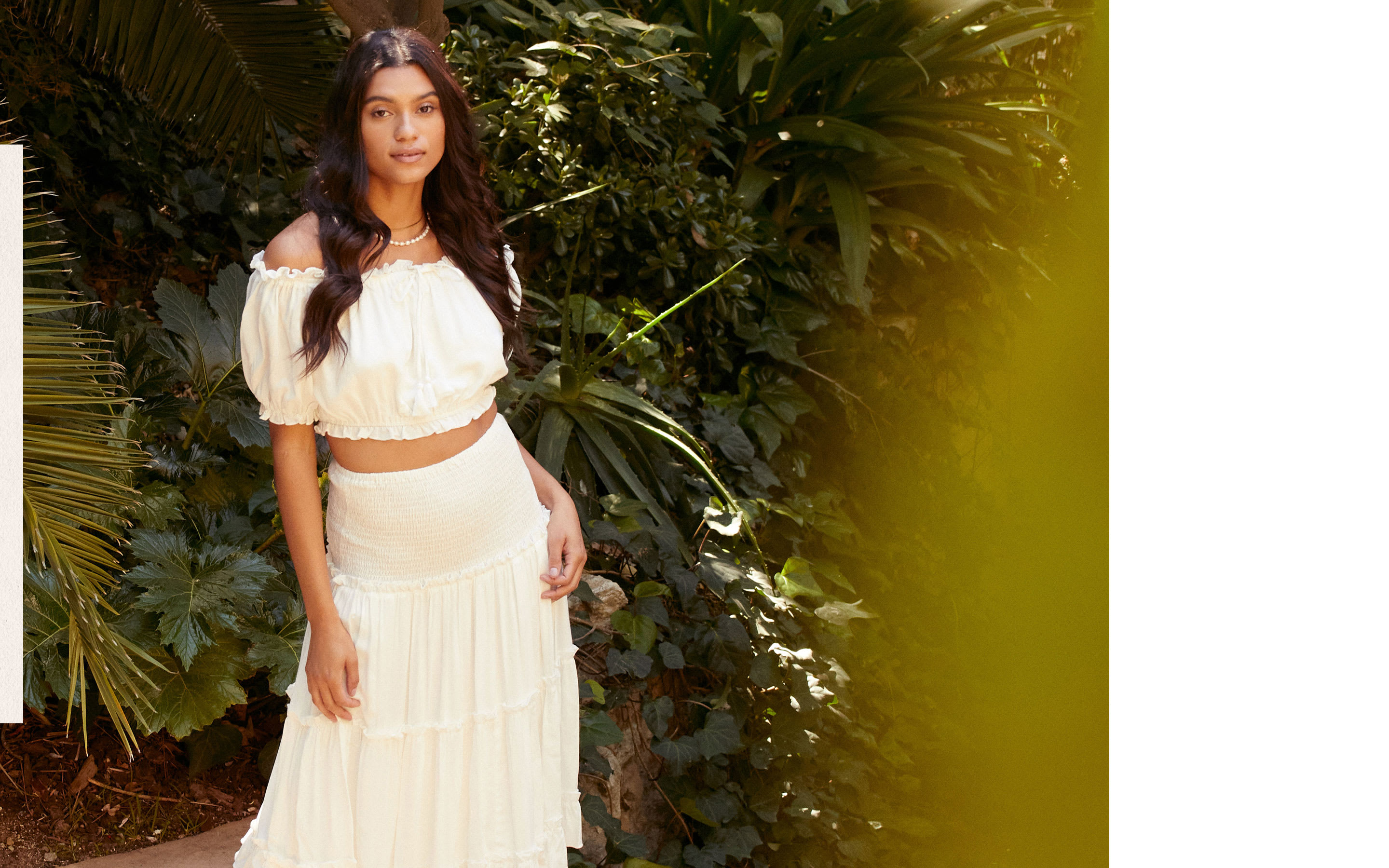 Model wearing white off-the-shoulder crop top and tiered midi skirt