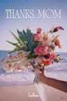 The gift card image, showing the text "Thanks, Mom" in white serif lettering, over a photo of a hand holding a colorful bouquet of roses, orchids, gerbera daisies, and tropical foliage, with the ocean and beach in the background