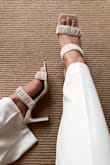 Comfortable and versatile. These cute little off white heels are going to be a staple in my spring/summer wardrobe. The blade heel and ruched straps are very trendy right now without being quite as bulky as some other styles, and are more flattering for larger feet. I'm usually between a 10-11 with very narrow feet, and I always order a 10 in this style of shoe. I found these to run a little on the narrow side in the 10, compared to other shoes from Lulus in this size and style, but since my feet are narrow, this isn't a problem for me. It does help keep my feet from sliding all the way forward, which is nice. They look chic with my off-white crepe wide leg pants, perfect for a cocktail party by the beach! - Phoebe E.