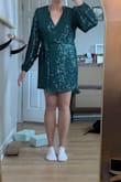 I was a little nervous ordering this dress because it's definitely on the short side, but I'm actually really happy with it. The green sparkly fabric is gorgeous in person. It catches the light beautifully without looking cheap or overly glittery. It feels like the perfect statement piece for a night out or a party. Length wise, it's very short, but it technically passes the sit test for me. My bare bottom doesn't touch the seat when I sit down. That said, I personally felt more comfortable wearing bike shorts underneath. They don't show at all, which made it easy to move around without worrying. I also tried on the square neck version, but I ended up preferring this wrap style. The wrap cut is just a little bit longer and gives a bit more coverage, which made a noticeable difference. It's still flirty and fitted, but slightly more practical. Overall, if you're okay with a mini dress and want something sparkly and fun, this one is a great pick. Just keep in mind the length and consider shorts underneath. - Erin K.