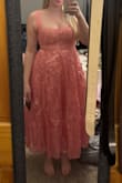 I'm not a fan of how "poofy" the bottom half is, but maybe it's because I'm bigger than the model in the picture and curvier, so that could just be how it sits on my body. The dress is more of a peach or salmon tone rather than the bright pink (I swear it's not just the lighting of my pics). It feels very cheap and honestly looks cheap too. I felt like the lace up back was going to snap the whole time. I do like the corset back because it does hold your boobs for you without needing a bra, but the overall fit is just weird. The fabric feels like plastic, and it's rough. - Clair U.