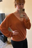 Edit: this is still amazing but it will shed!! On anything you wear it with and on anything you wash it with so be aware. Doesn't shrink in the wash. I hope they make more colors because this is the perfect sweater I always dreamed of. This is a true orange and not a weird brown. Typically I'm picky with sweaters and most materials irritate my sensitive skin. This is the softest material ever! I ordered my regular S. I could've done a XS because it's very loose, but then it would've been a crop. This hits right at the hips and the tighter seam on the bottom keeps it in place around my hips unless I raise my hands completely up and then it rides up a little. The sleeves are almost like balloon sleeves (which I normally hate) but these drop shoulders and loose material just make you look cute like you're tiny in a looser sweater. I also love how the v neck is the perfect amount of revealing if you want it to be. - Katie B.