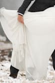 I wore this for my fall elopement in the mountains, even hiked in it! The dress is of high quality and is very durable. (I was able to gather the skirt in the front and tie it up for ease of movement while hiking.) It is not thin, but actually heavy, with 3 full layers. There is a satin underlayer, a solid shell layer and one more shell layer made of two pieces that cascade and meet high in the middle at the bust. 
I had enough room to wear undergarments and fleece-lined tights to stay warm. It fit me in the bust after an easy hem to close the gap, but I had to have it altered due to my abdomen. The hip area is forgiving and is not fitted. The seamstress let out the waist and replaced the zipper with a beautiful satin corset tie and it worked so well for me! The skirt is very flowy and translates well for dramatic photo poses as others before me have stated. - Nicole L.